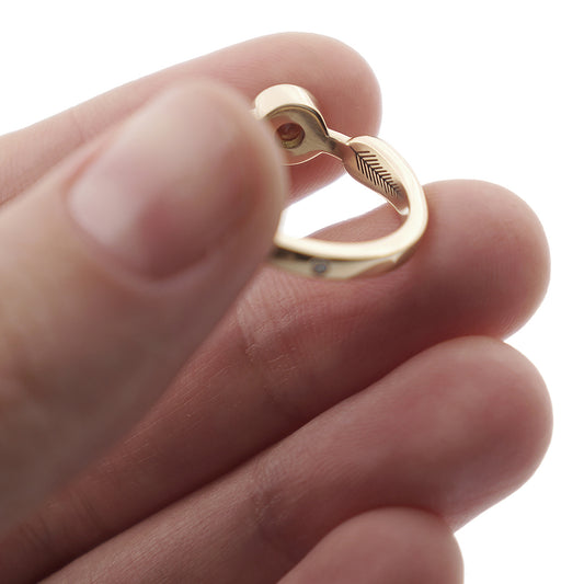 A close-up of a yellow gold engagement ring with a diamond and laser-engraving in a woman's hand.
