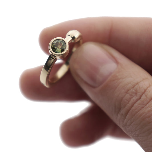 A close-up of a yellow gold engagement ring with a pale green sapphire in a woman's hand.