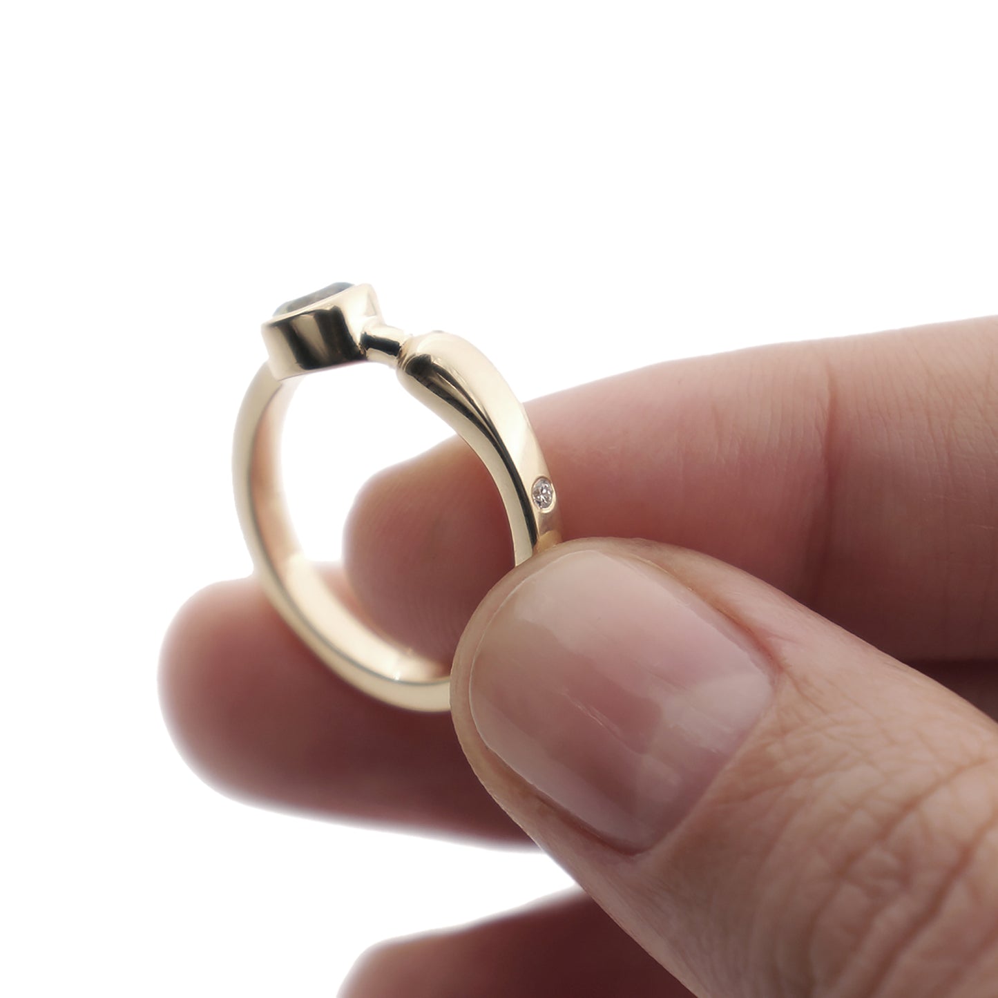 A close-up of a yellow gold engagement ring with a pale green sapphire and a diamond in a woman's hand.
