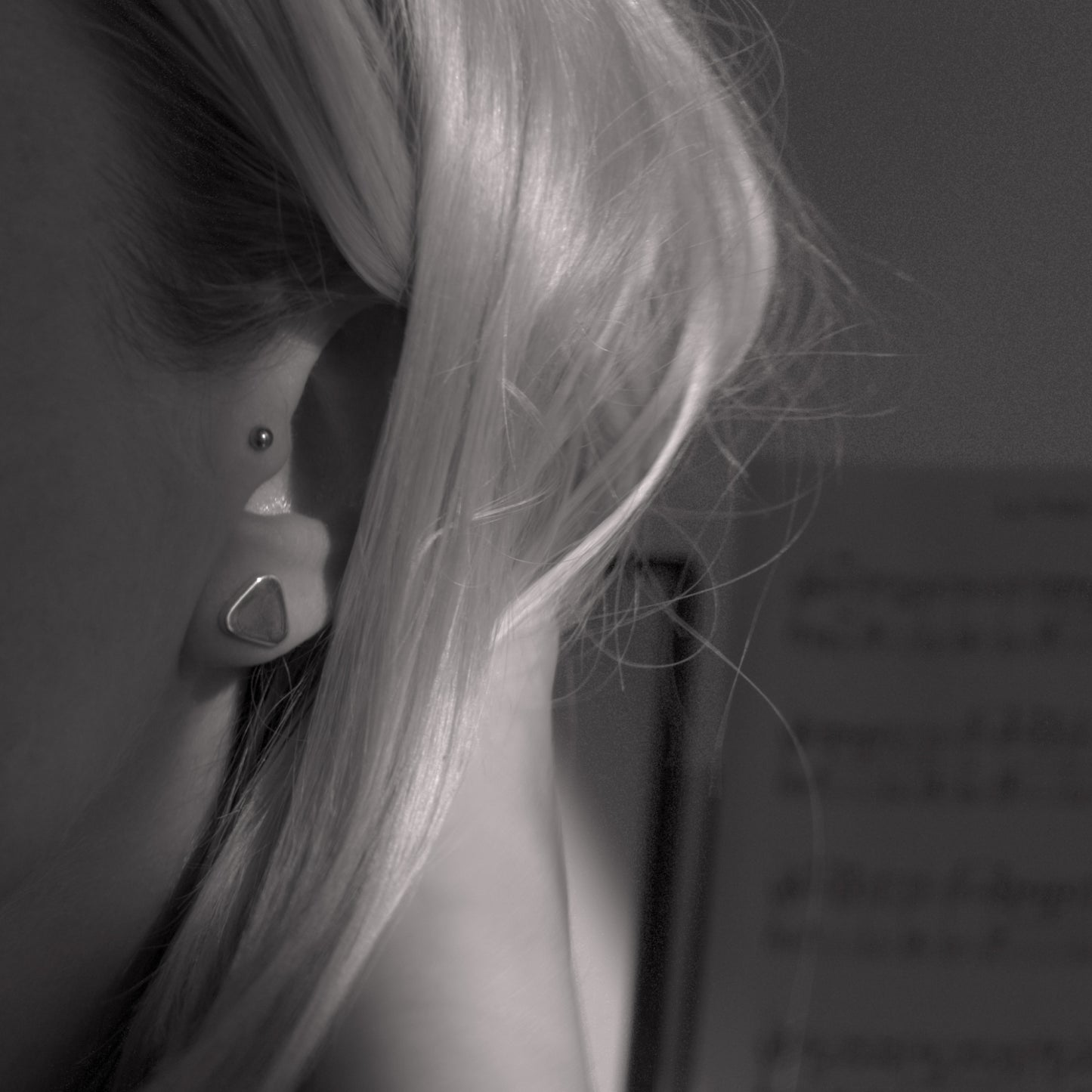 A close-up of a minimalist design silver earring in a soft triangular shape in a woman's ear. Black and white.