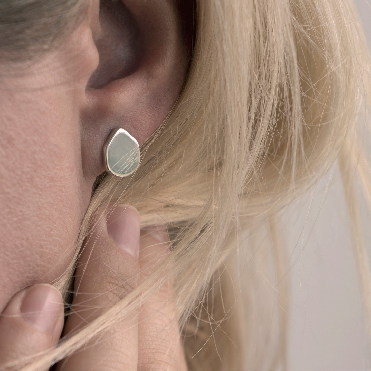 A close-up of a minimalist earring with an organic shape in a woman's ear.