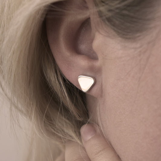A close-up of a minimalist design silver earring in a soft triangular shape in a woman's ear.