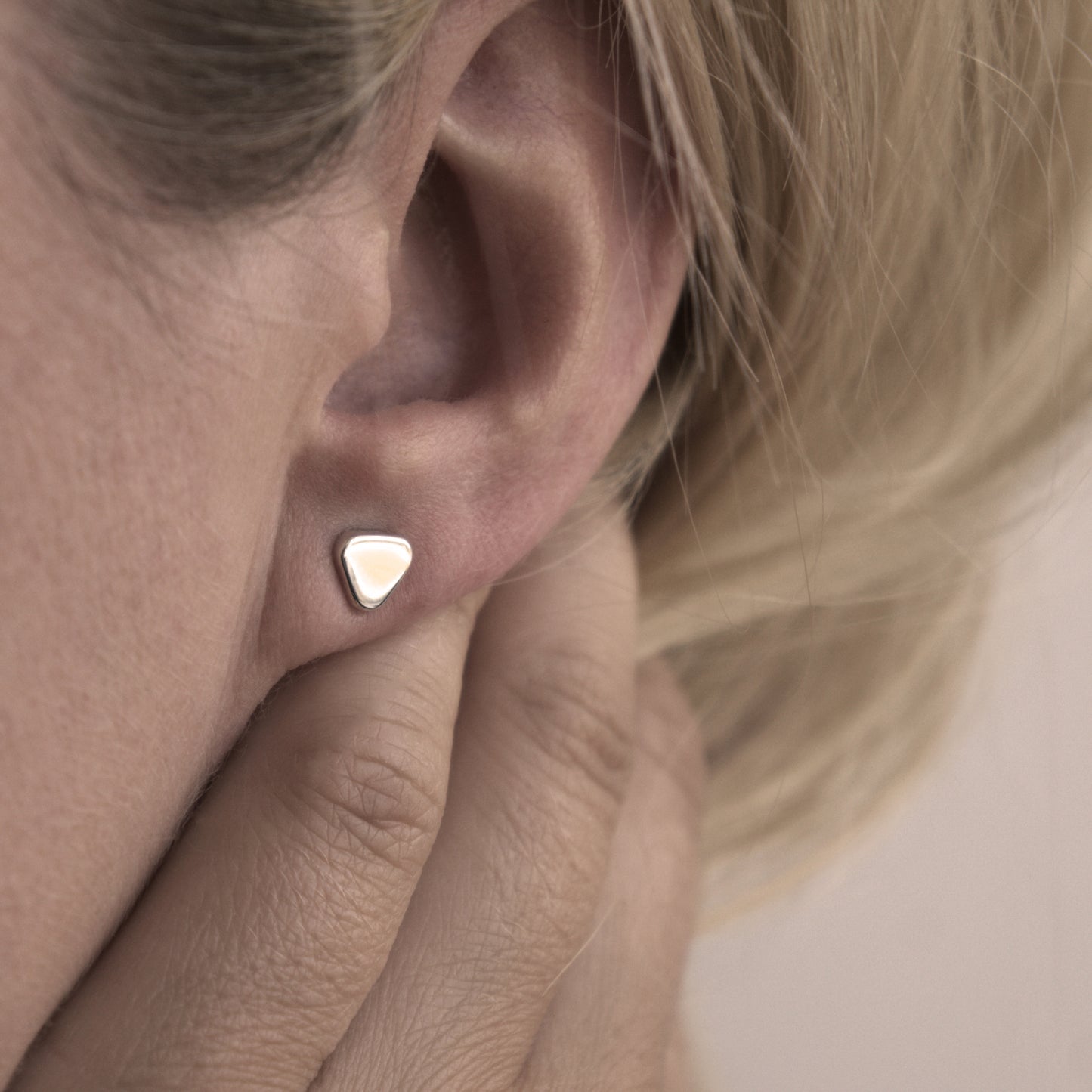 A close-up of a small minimalist design silver earring in a soft triangular shape in a woman's ear.