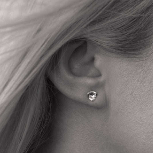 A close-up of a small silver earring in a minimalist, organic shape in a woman's ear. Black and white.