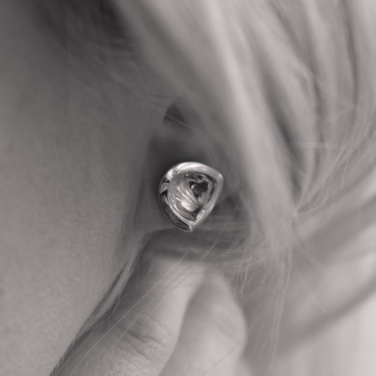 A close-up of a silver earring in a minimalist, organic shape in a woman's ear. Black and white.