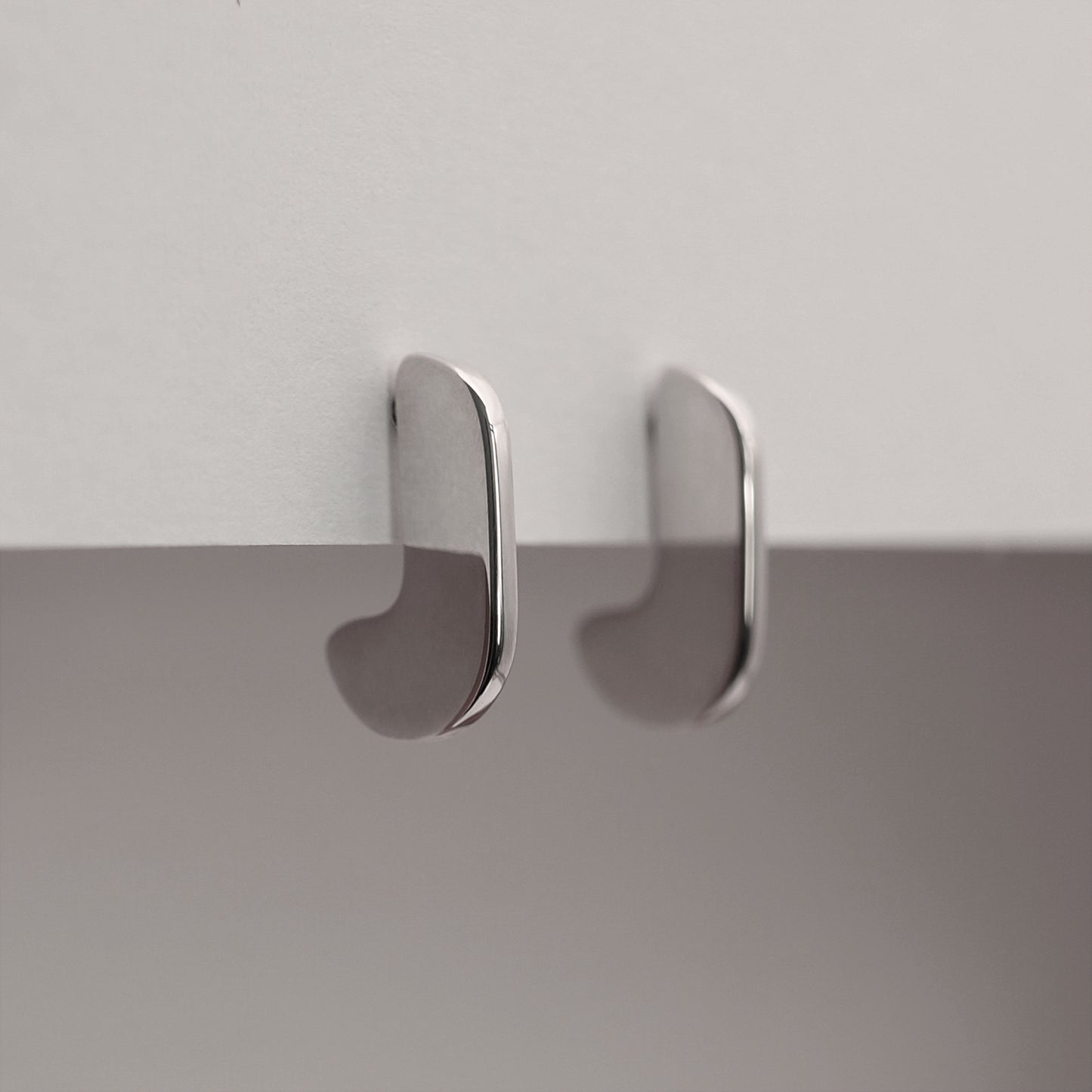 A side view of a pair of silver earrings with an organic shape and minimalist design.