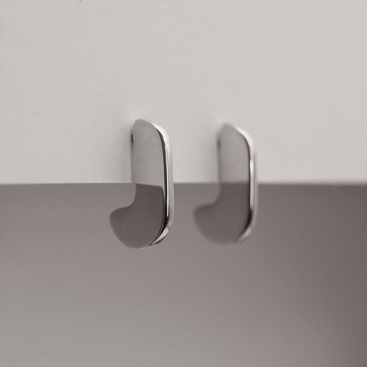A side view of a pair of silver earrings with an organic shape and minimalist design.