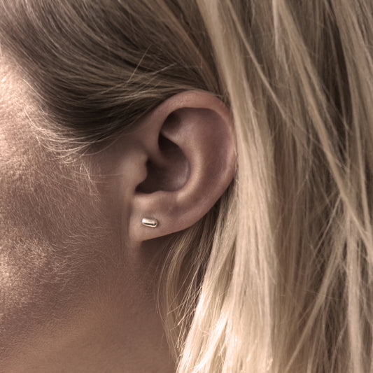 A close-up of a silver earring with a minimalist design in a capsule shape in woman's ear.