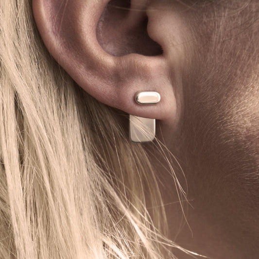 A close-up of a minimalist silver earring in a woman's ear.