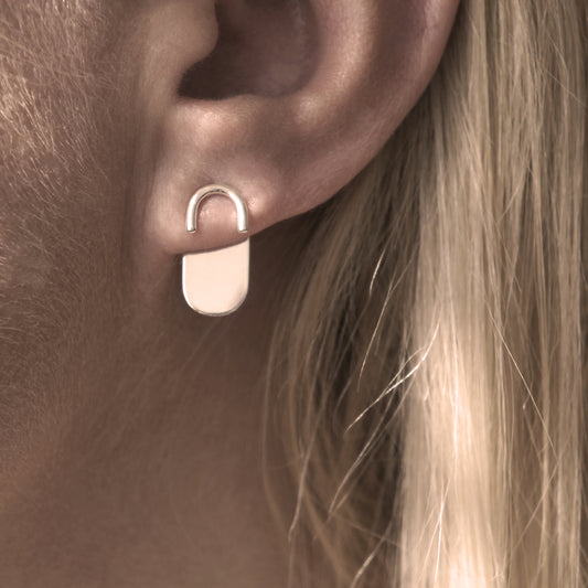 A close-up of a minimalist silver earring in a woman's ear.