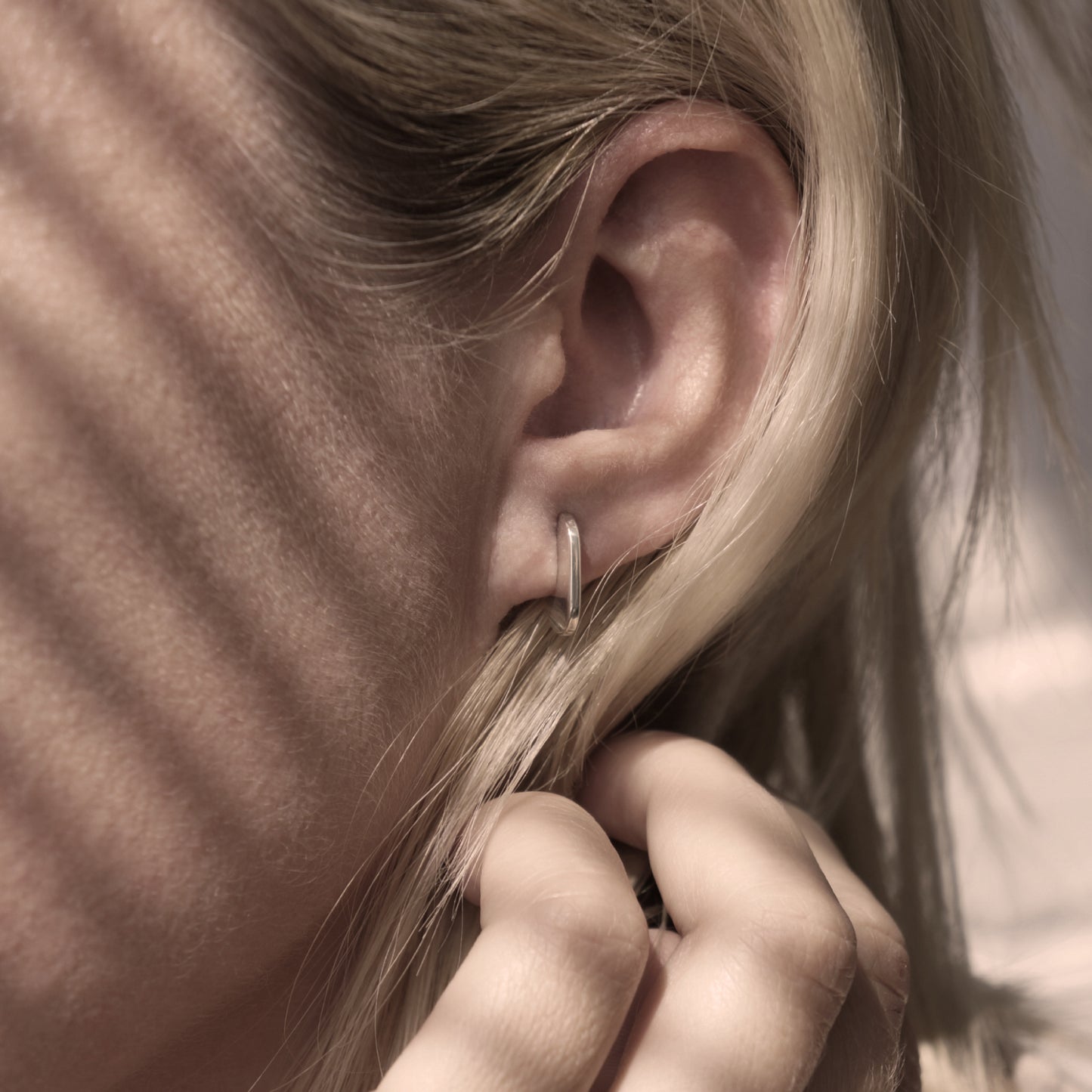 A close up of a minimalist design silver earring in a woman's ear.
