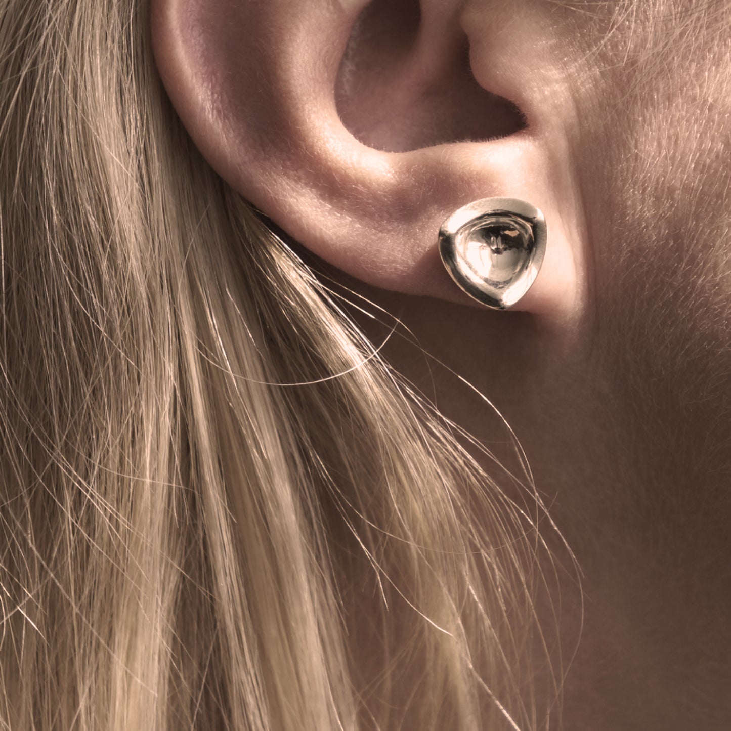 A close-up of a silver earring in a minimalist, organic shape in a woman's ear.
