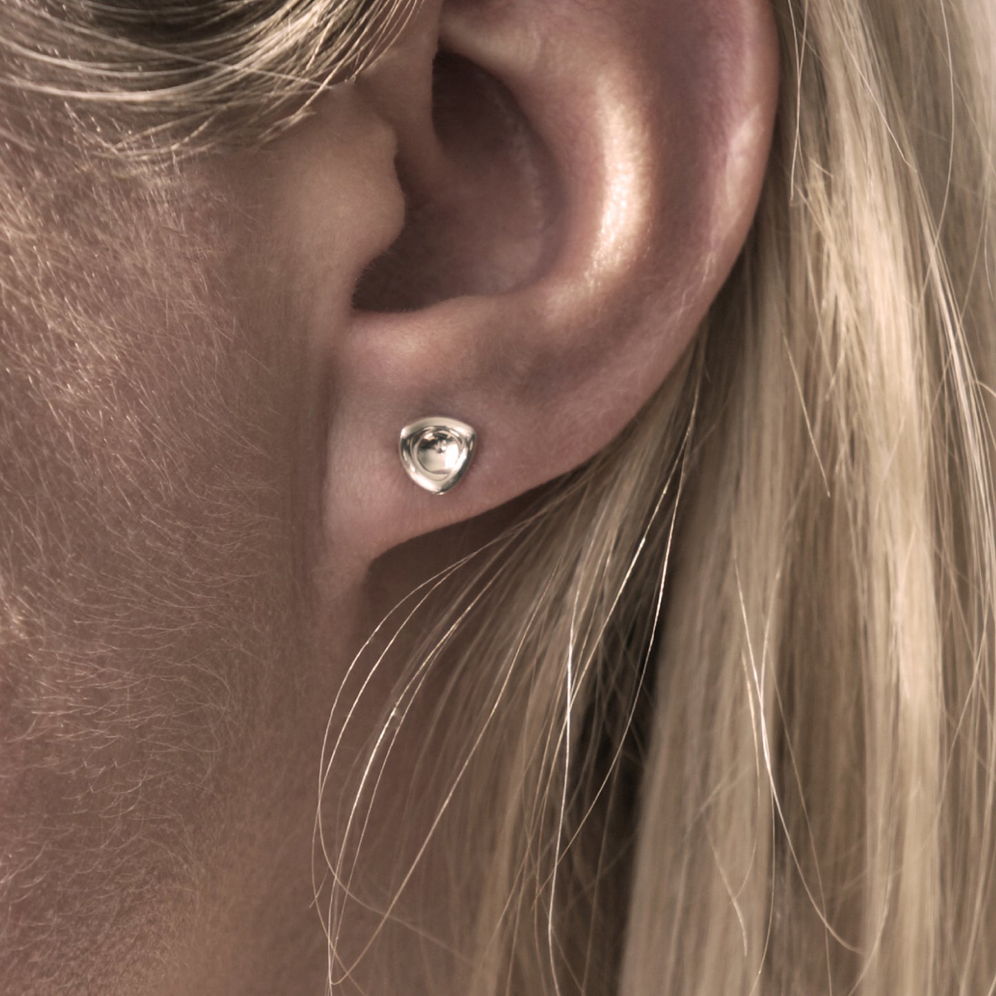 A close-up of a small silver earring in a minimalist, organic shape in a woman's ear.