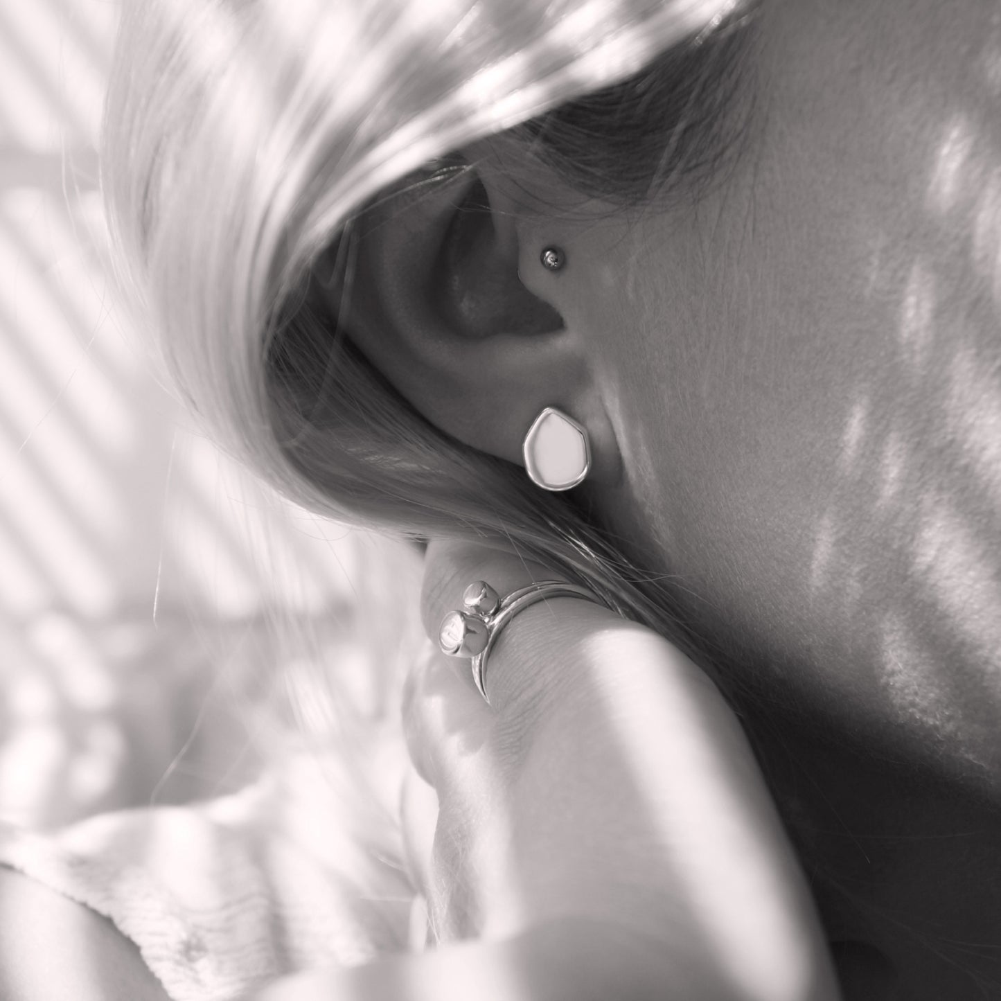 A close-up of a minimalist earring with an organic shape in a woman's ear. Black and white.