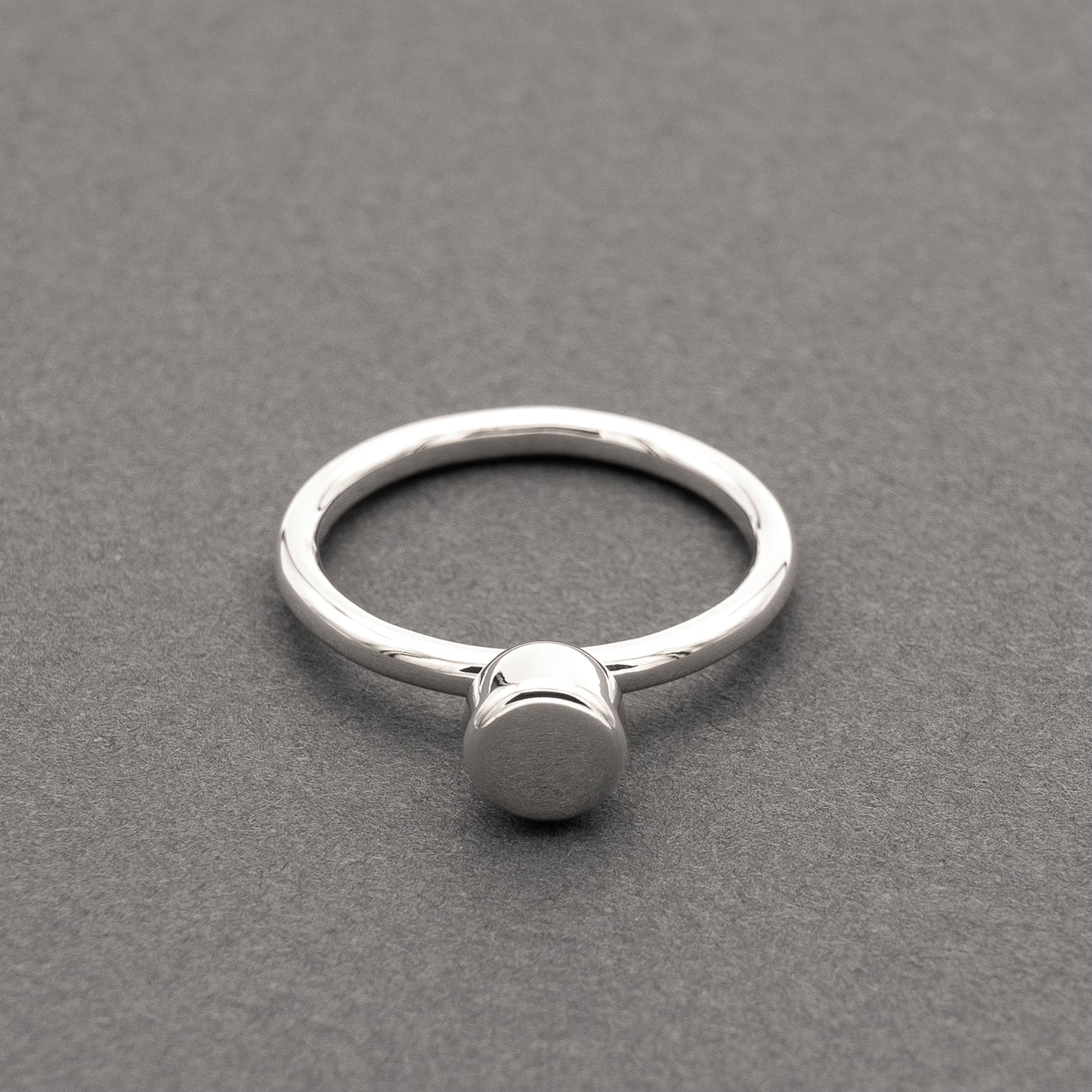 A front view of a silver ring with a minimalist design and a half-capsule element.