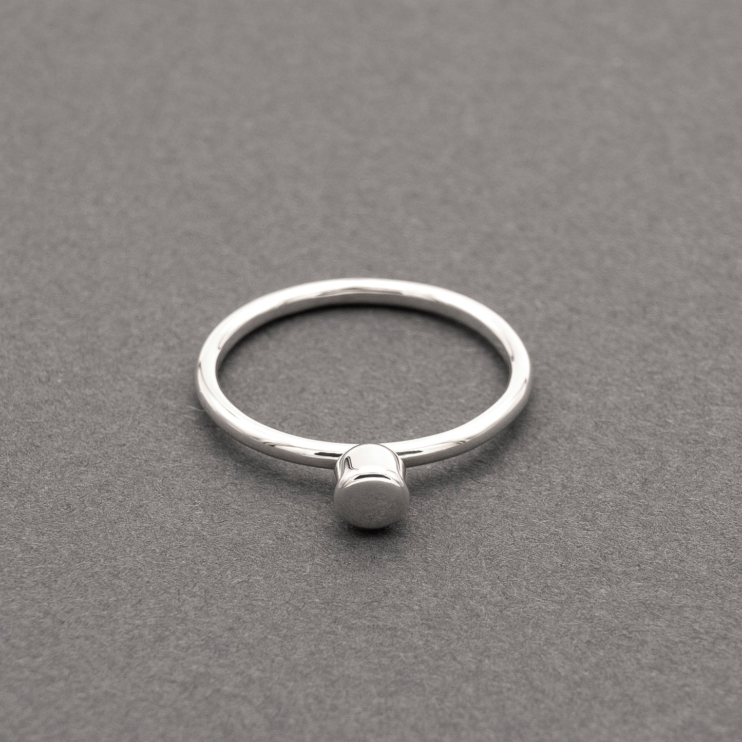 A front view of a silver ring with a minimalist design and a small half-capsule element.