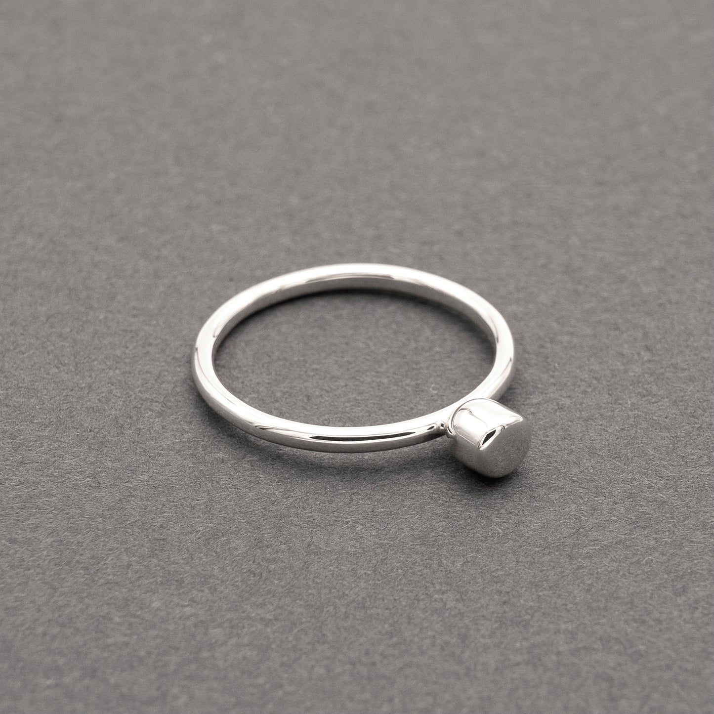 A slight side view of a silver ring with a minimalist design and a small half-capsule element.