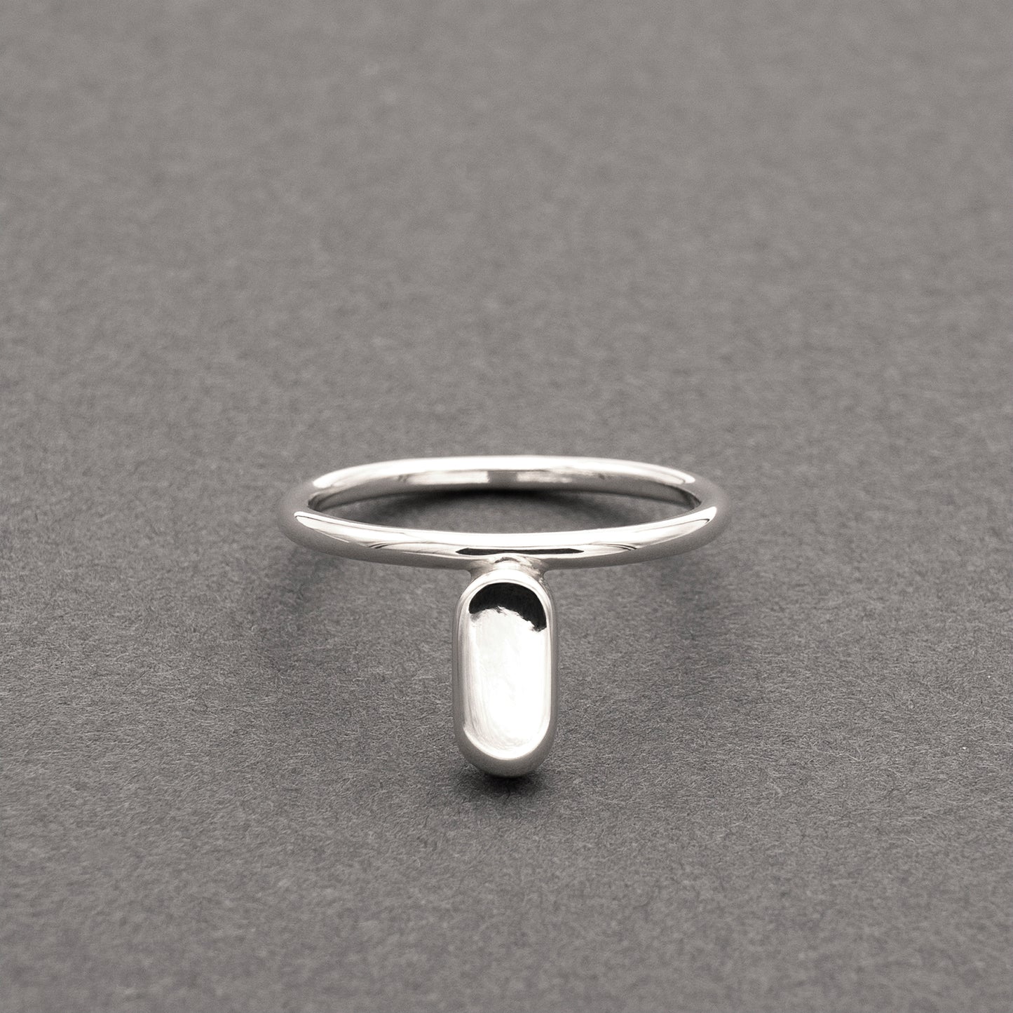 A front view of a silver ring with a minimalist design and a flat capsule element.
