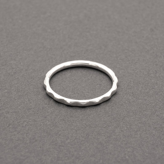 Minimalist design thin silver ring with a wavy texture, displayed on a grey background.