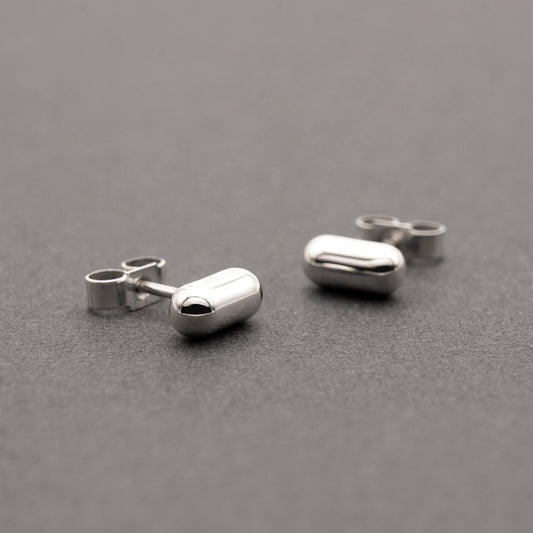 Two silver earrings with a minimalist design in a capsule shape.