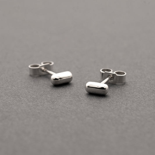 Two silver earrings with a minimalist design in a capsule shape.