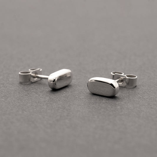 Two silver earrings with a minimalist design in a flat capsule shape.