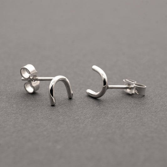 A close-up of two minimalistic silver horseshoe-shaped earrings.