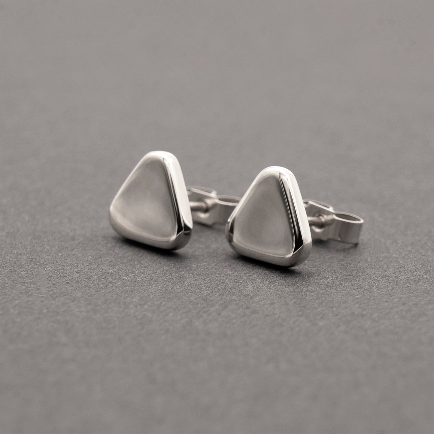 A slight side view of two minimalist design silver earrings in a soft triangular shape.