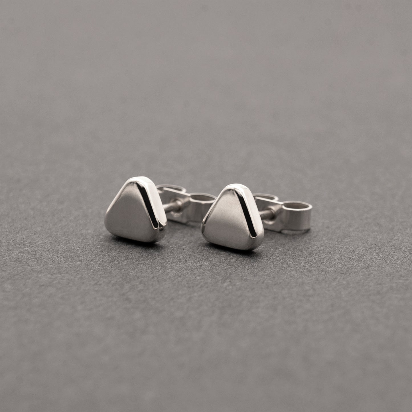 A slight side view of two small minimalist design silver earrings in a soft triangular shape.