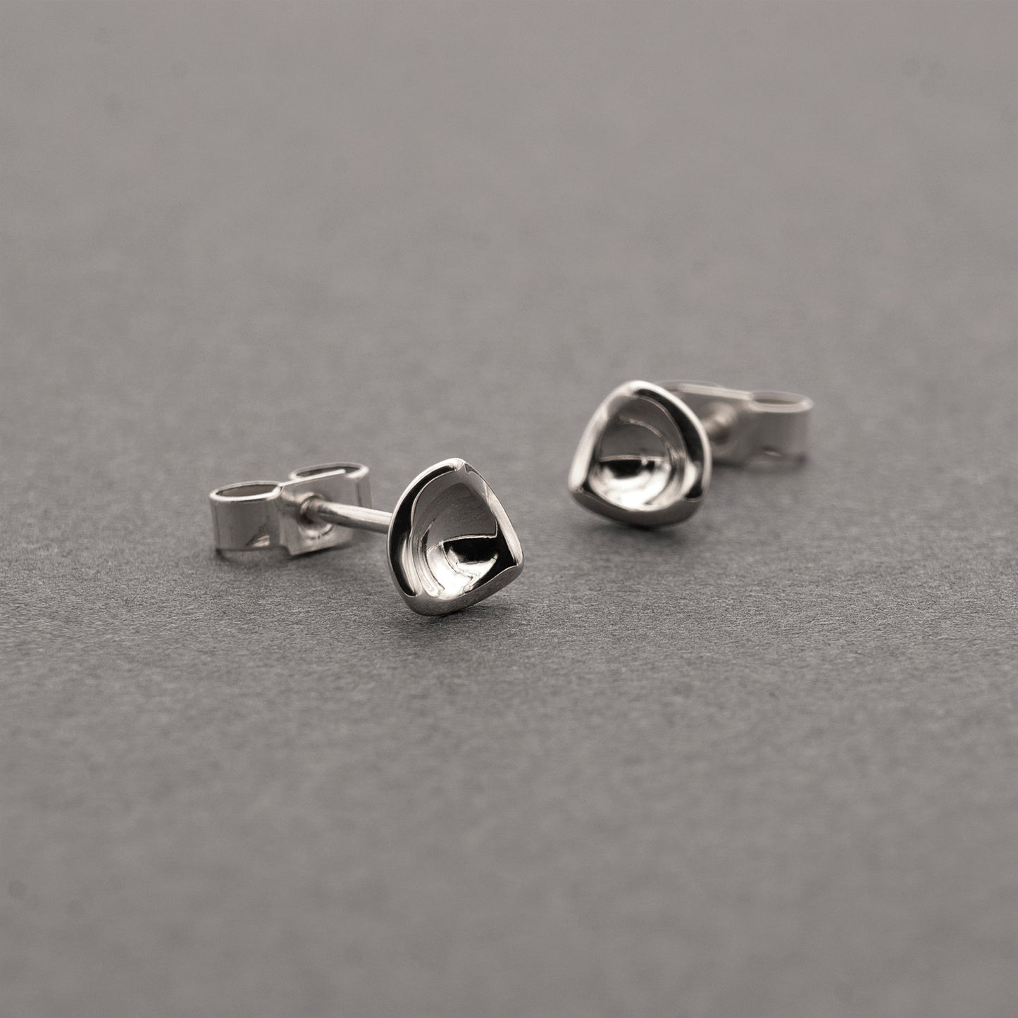 Two small silver earrings in a minimalist, organic shape.