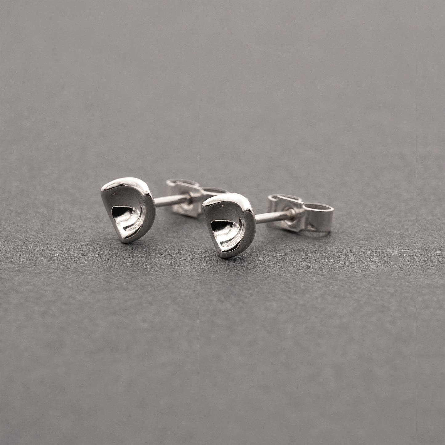 A slight side view of two small silver earrings in a minimalist, organic shape.