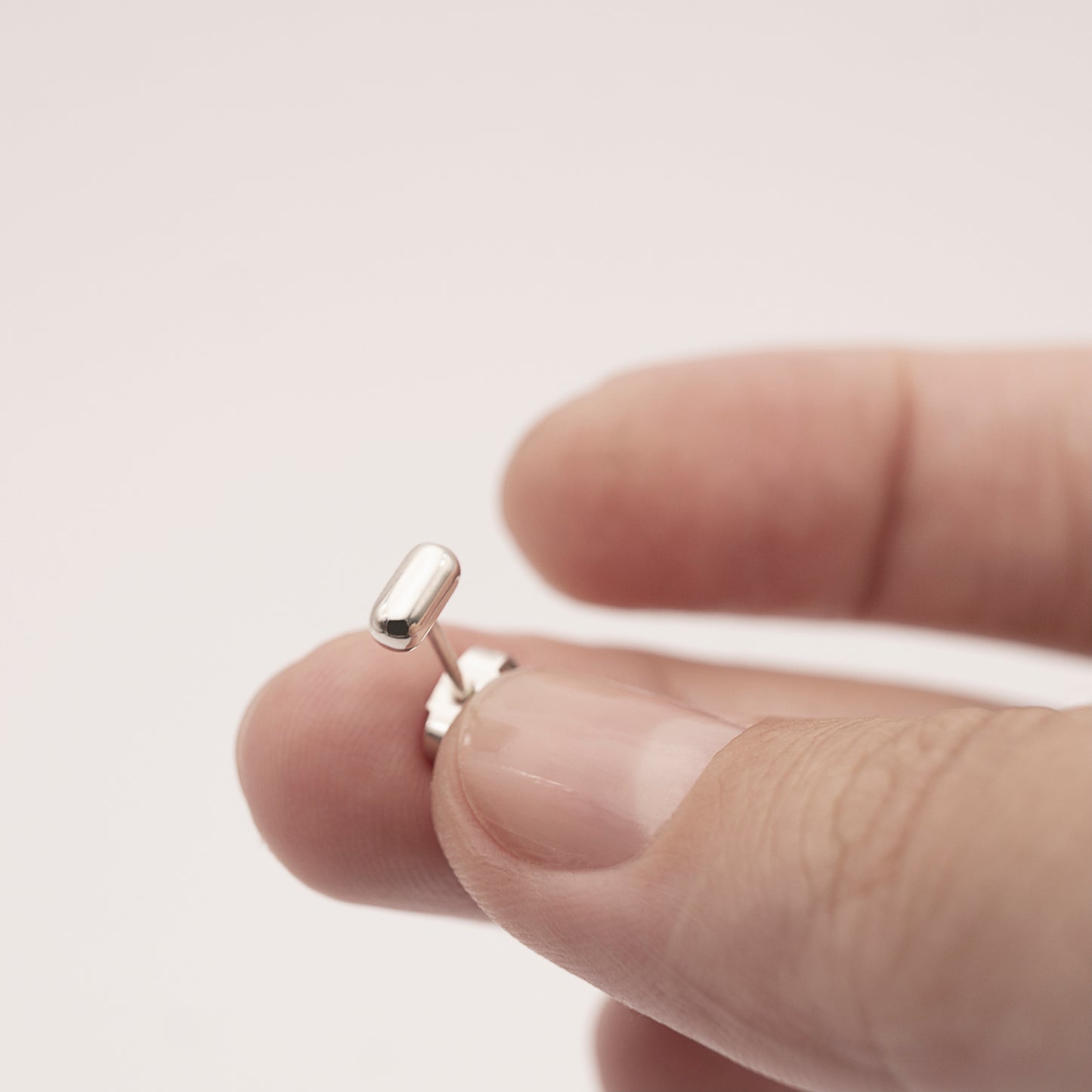 A close-up of a silver earring with a minimalist design in a capsule shape in woman's hand.