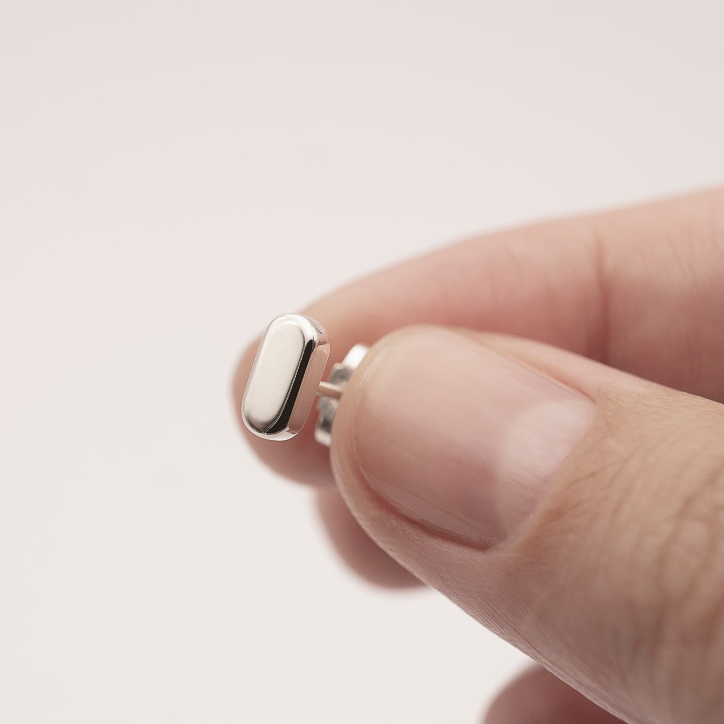 A close-up of a silver earring with a minimalist design in a flat capsule shape in a woman's hand.