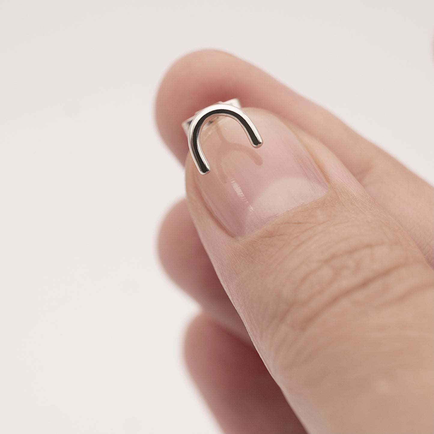 A close-up of a minimalistic silver horseshoe-shaped earring in a woman's hand.