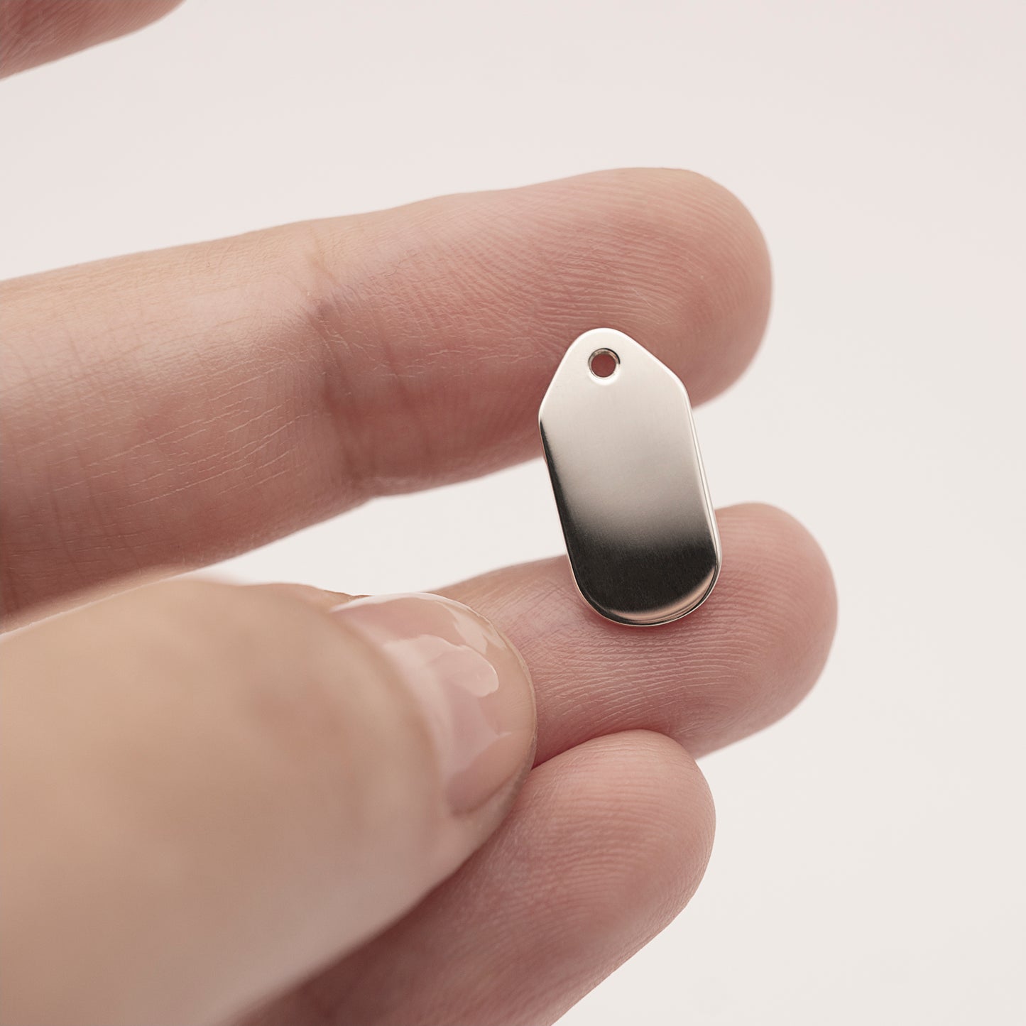 A close-up of a minimalist silver earring backplate in a woman's hand.