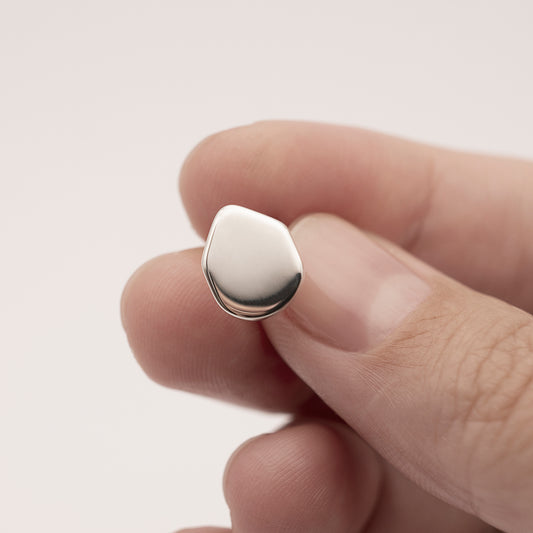 A close-up of a silver earring with a minimalist design in a person's hand.