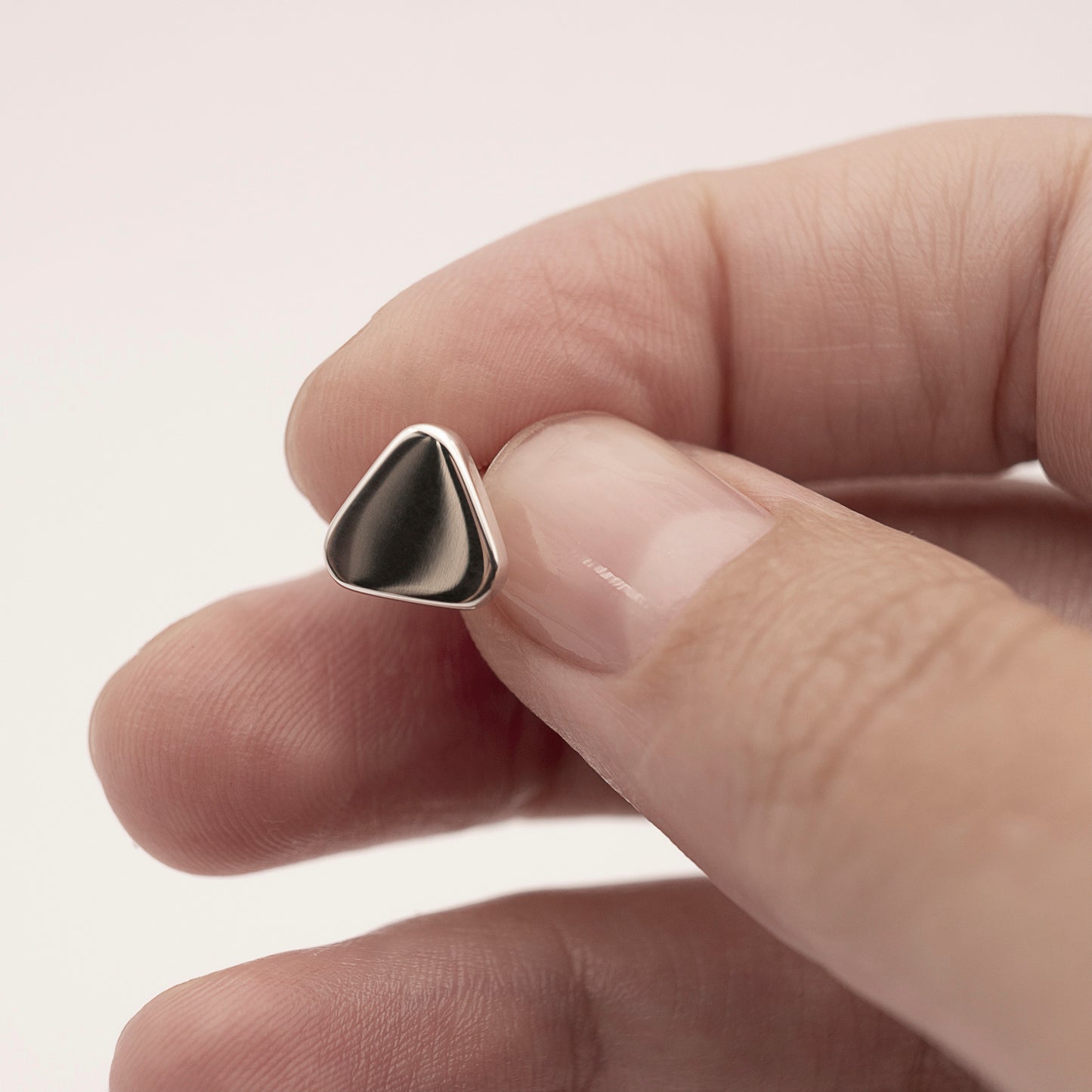 A close-up of a minimalist design silver earring in a soft triangular shape in a woman's hand.