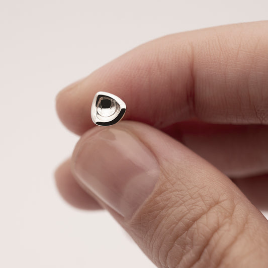 A close-up of a small silver earring in a minimalist, organic shape in a woman's hand.