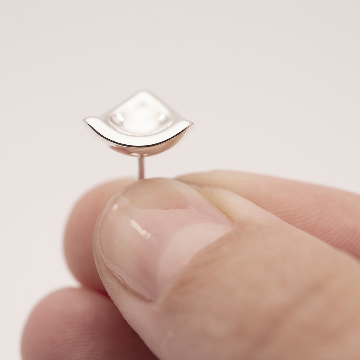 A close-up of a silver earring in a minimalist, organic shape in a woman's hand.