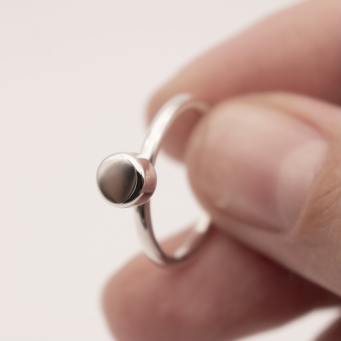 A close-up of a minimalist design silver ring with a half-capsule element in a woman's hand.