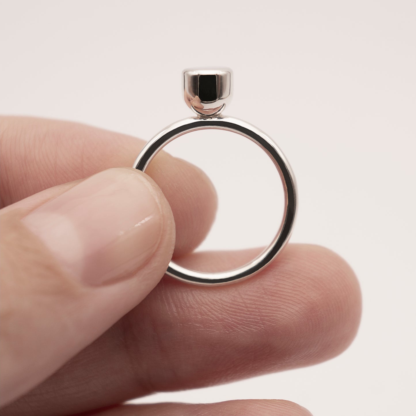 A close-up, front view of a silver ring with a minimalist design and a half-capsule element in a woman's hand.
