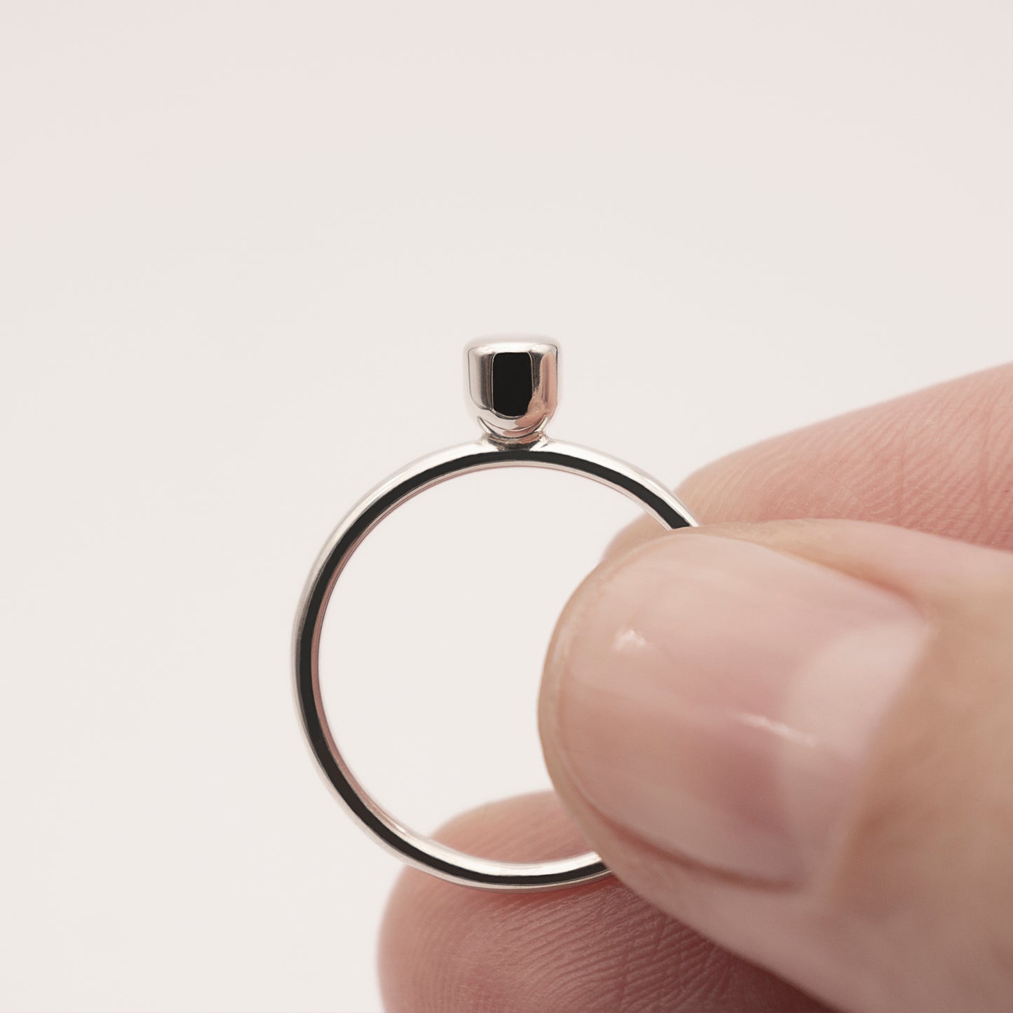 A close-up, front view of a silver ring with a minimalist design and a small half-capsule element in a woman's hand.