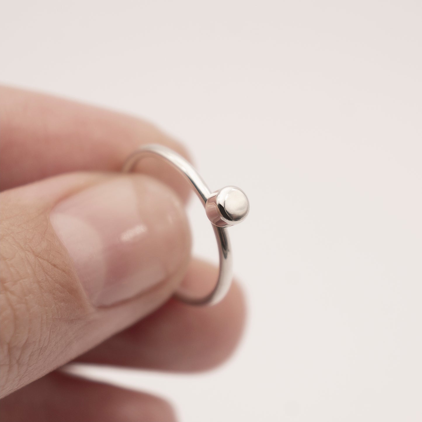 A close-up of a minimalist design silver ring with a small half-capsule element in a woman's hand.