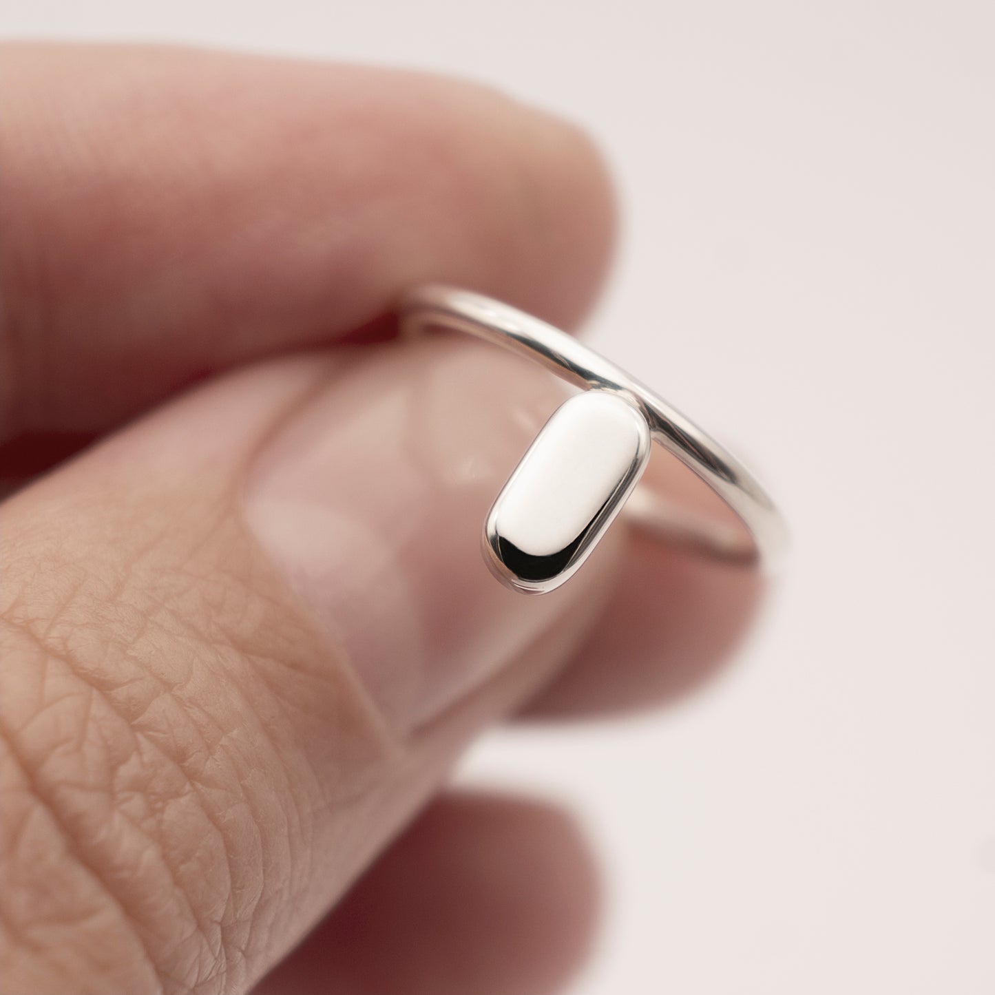 A close-up of a silver ring with a minimalist design and a flat capsule element in a woman's hand.