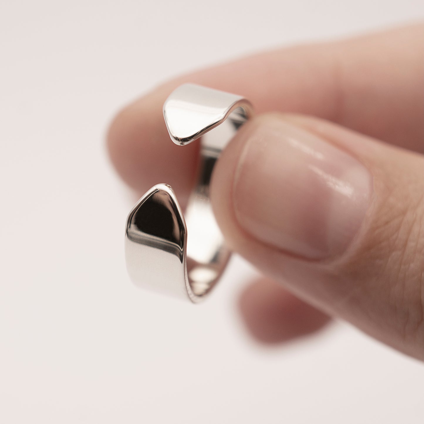 A close-up of a minimalist design wide band ring in silver in a woman's hand.