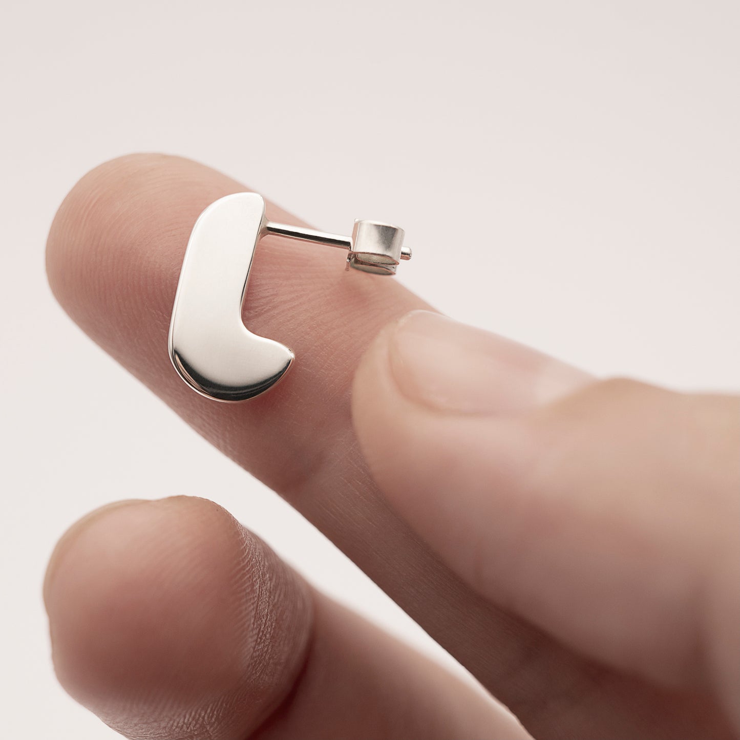 A close-up of a minimalist design silver earring on a person's finger.