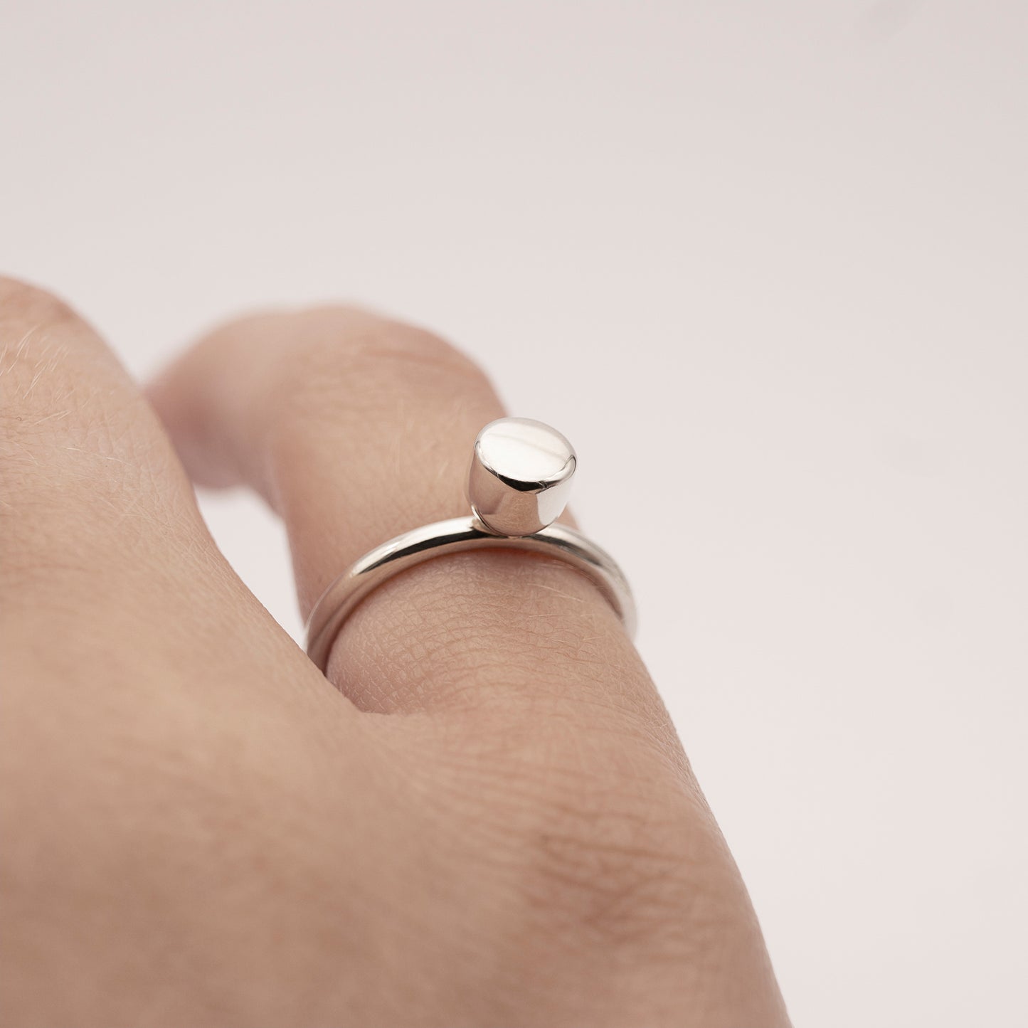 A close-up of a minimalist design silver ring with a half-capsule element on a woman's little finger.