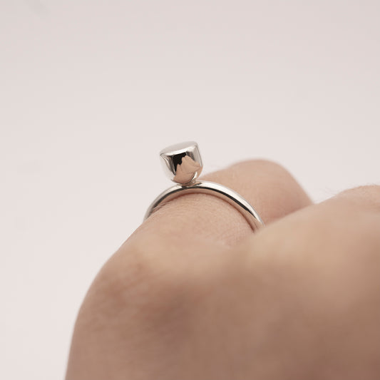 A close-up of a minimalist design silver ring with a half-capsule element on a woman's little finger.