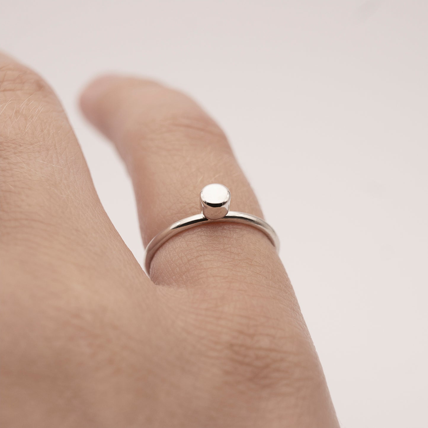 A close-up of a minimalist design silver ring with a small half-capsule element on a woman's little finger.