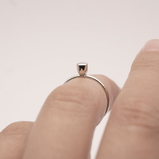 A close-up of a silver ring with a minimalist design and a small half-capsule element on a woman's index finger above the knuckle.